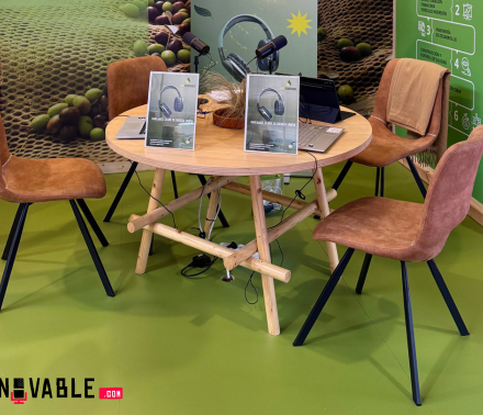 una mesa con cuatro sillas alrededor con dos tablets y dos microfonos sobre la mesa en un stand de feria ENOMAQ 2025