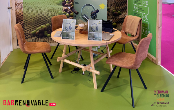 una mesa con cuatro sillas alrededor con dos tablets y dos microfonos sobre la mesa en un stand de feria ENOMAQ 2025