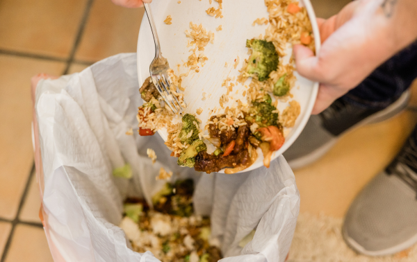 manos humanas vertiendo restos de comida en un cubo de basura